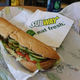 Subway footlong sandwich, bag of Doritos, and a bottle of water on Subway tabletop